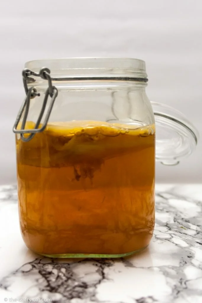 a mason jar with kombucha and a scoby standing on a marble table